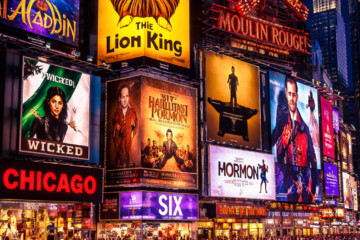 Times Square en Nueva York iluminado de noche, con carteles de musicales de Broadway como The Lion King, Wicked y Aladdin, rodeado de multitudes y taxis en un ambiente vibrante y turístico.
